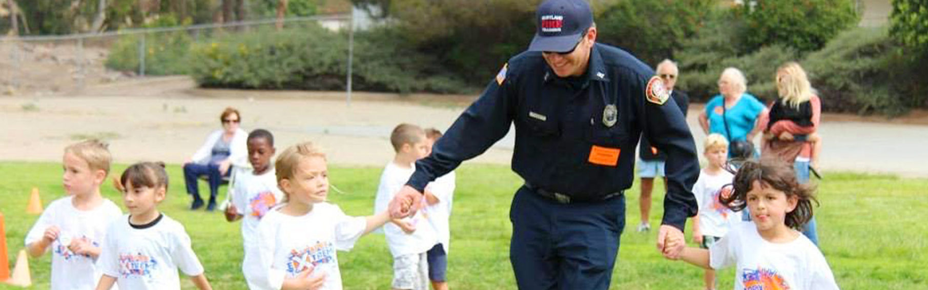 kids hold firefighter's hands while they run on a grassy field