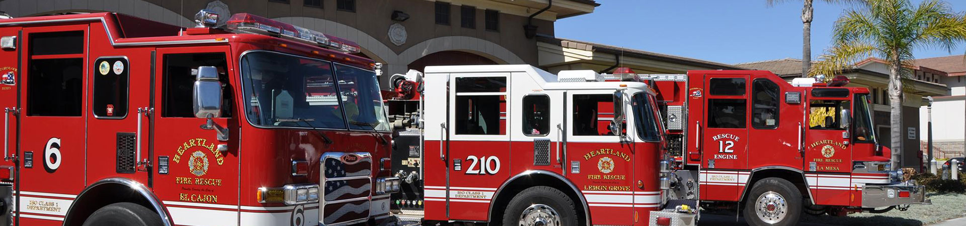 Three firetrucks outside fire station with palm trees in the sun